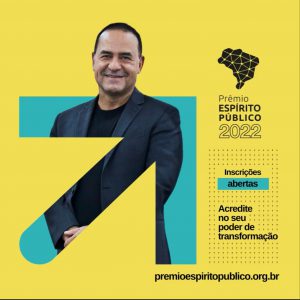 A arte tem um fundo amarelo com uma seta em verde apontando pra direita e pra cima. Da seta, sai a foto de um homem com cabelo baixo e sorrindo. Ao lado direito da arte, vemos um mapa do Brasil em preto e, abaixo, se lê "Prêmio Espírito Público 2022, inscrições abertas. Acredite no seu poder de transformação"