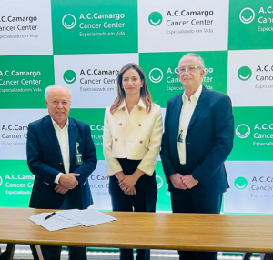 A foto mostra três pessoas, sendo dois homens e uma mulher, posando para a foto após a assinatura de um contrato